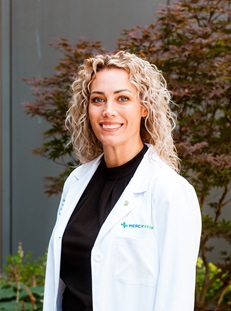 Dr. Tenkman, female appearance in a white lab coat with long curly hair.